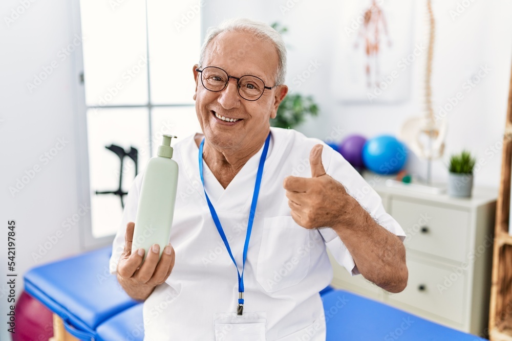 Senior physiotherapy man holding massage body lotion smiling happy and positive, thumb up doing excellent and approval sign