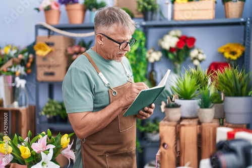 Middle age grey-haired man florist writing on notebook at flower shop