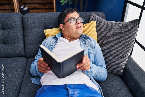 Down syndrome man reading book lying on sofa at home