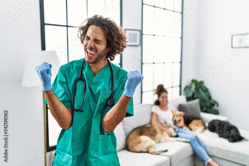 Young veterinarian man checking dogs at home very happy and excited doing winner gesture with arms raised, smiling and screaming for success. celebration concept. photo