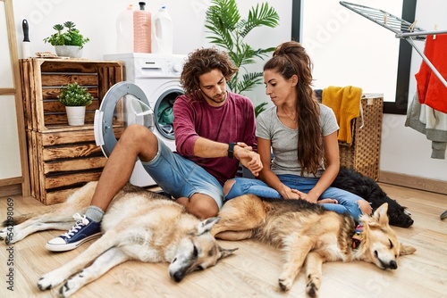Photography Young hispanic couple doing laundry with dogs checking the time on wrist watch,