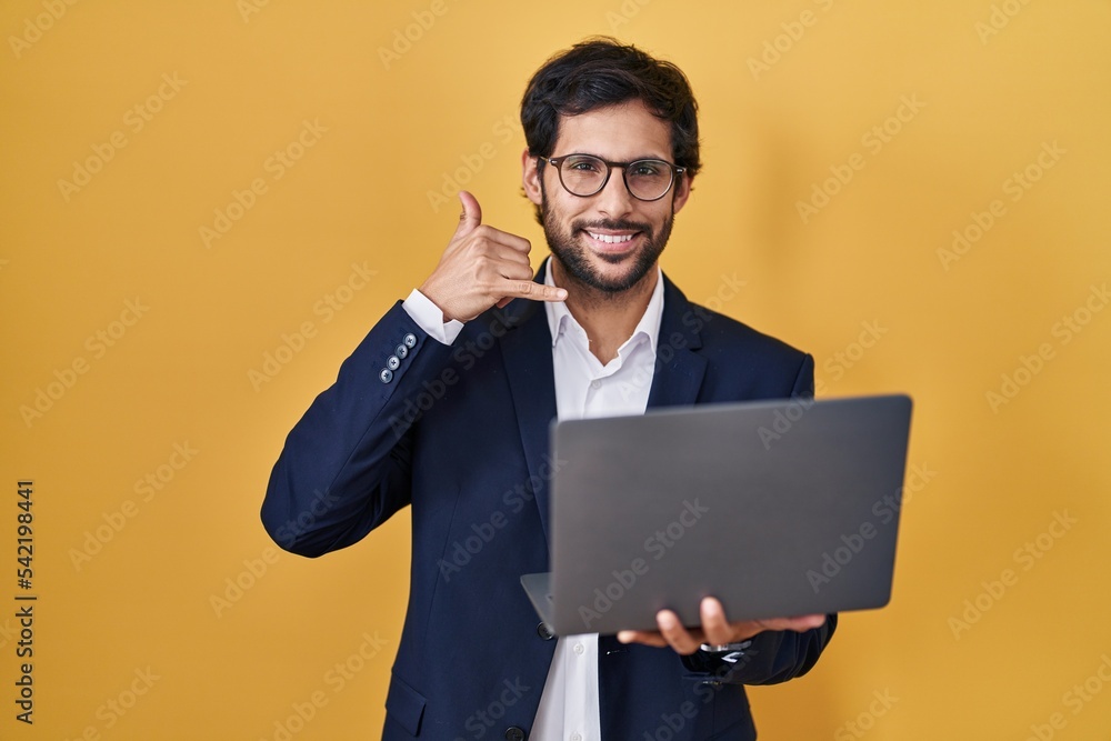 Handsome latin man working using computer laptop smiling doing phone gesture with hand and fingers like talking on the telephone. communicating concepts. Handsome latin man working using computer laptop smiling doing phone gesture with hand and fingers like talking on the telephone. communicating concepts.