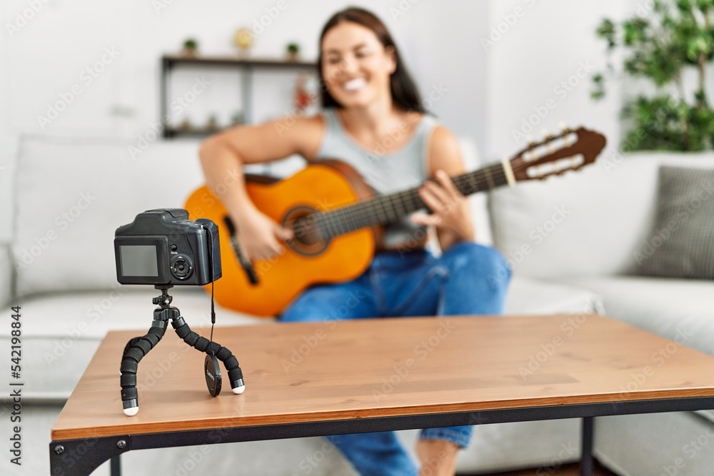 Fototapeta premium Young beautiful hispanic woman having playing classical guitar recording video at home
