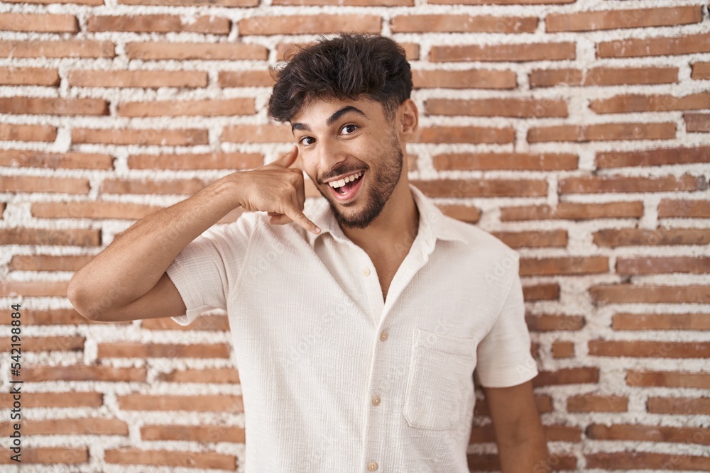 Arab man with beard standing over bricks wall background smiling doing phone gesture with hand and fingers like talking on the telephone. communicating concepts. Arab man with beard standing over bricks wall background smiling doing phone gesture with hand and fingers like talking on the telephone. communicating concepts.