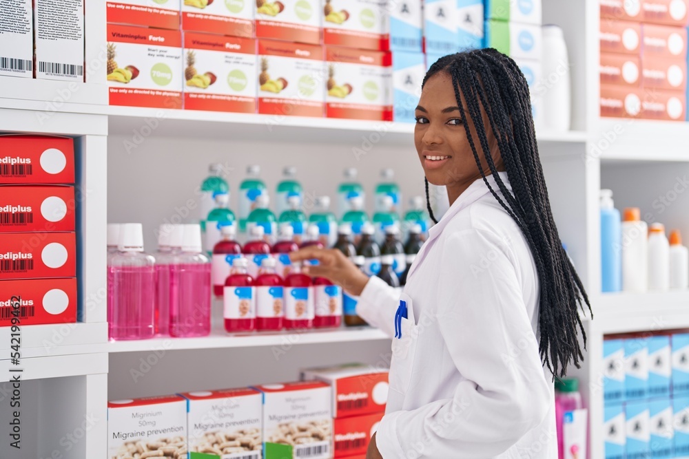 African american woman pharmacist smiling confident organizing shelving at pharmacy