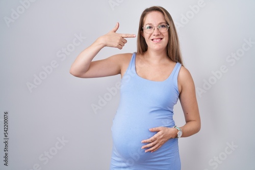 Young pregnant woman standing over white background smiling cheerful showing and pointing with fingers teeth and mouth. dental health concept.