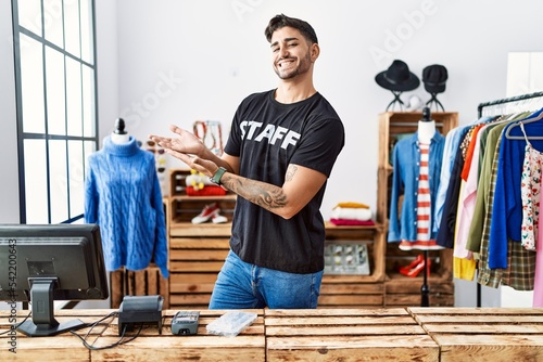 Young hispanic man working at retail boutique pointing aside with hands open palms showing copy space, presenting advertisement smiling excited happy