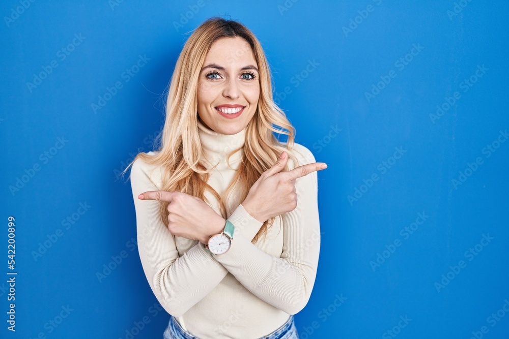 Young caucasian woman standing over blue background pointing to both sides with fingers, different direction disagree Young caucasian woman standing over blue background pointing to both sides with fingers, different direction disagree