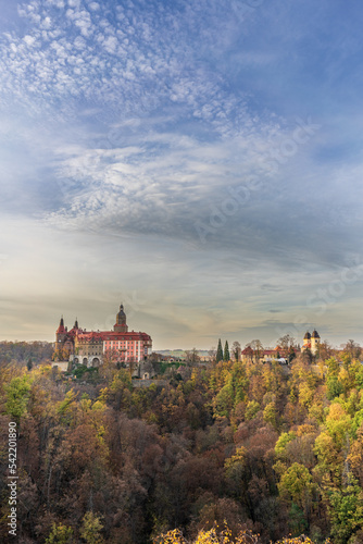 A photo of Książ Castle in Wałbrzych set against a beautiful autumn sky. The castle, with its impressive architecture, stands out against the picturesque background of the colorful fall foliage © Aleks