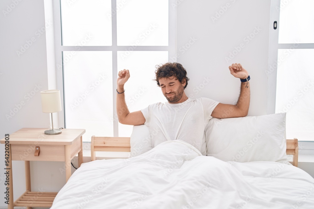 Young hispanic man waking up stretching arms at bedroom Young hispanic man waking up stretching arms at bedroom