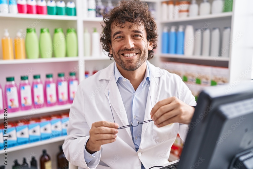 Young hispanic man pharmacist smiling confident using computer at pharmacy