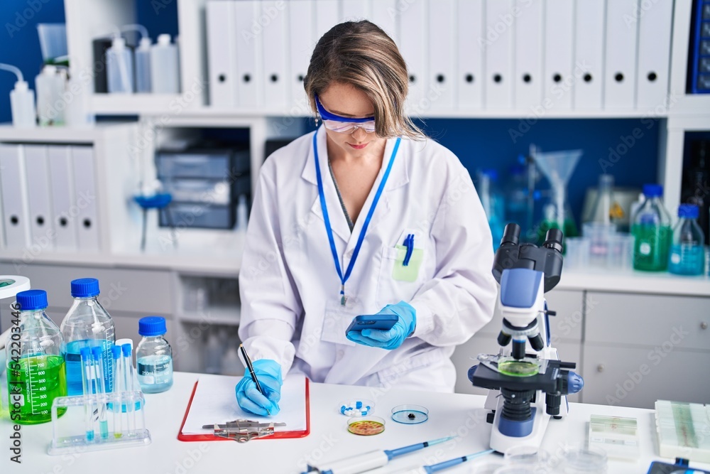 Young woman scientist writing report using smartphone at laboratory