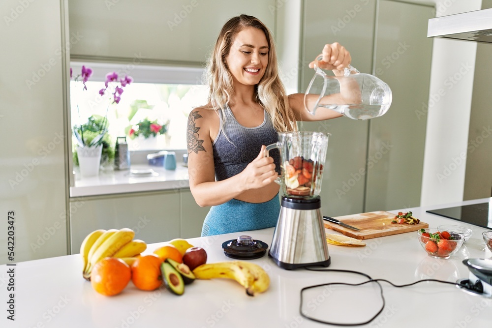 Young woman smiling confident pouring water on blender at kitchen Young woman smiling confident pouring water on blender at kitchen