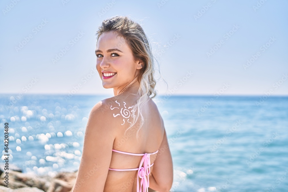 Young blonde girl with sunscreen sun draw on her back standing at the beach.