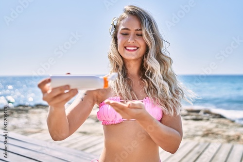 Young blonde girl wearing bikini using sunscreen lotion at the beach.