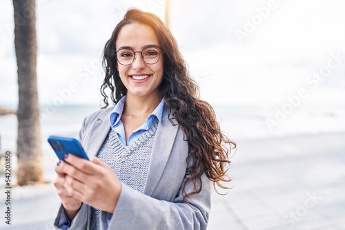 Young hispanic woman executive using smartphone at seaside