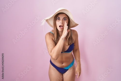 Young hispanic woman wearing bikini over pink background hand on mouth telling secret rumor, whispering malicious talk conversation