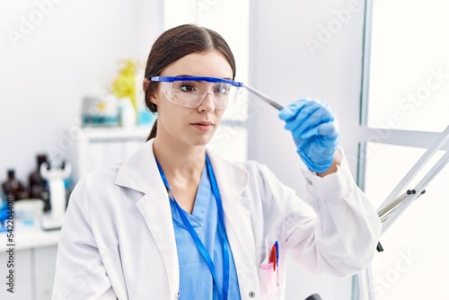Young hispanic woman wearing scientist uniform holding insect with tweezers at laboratory
