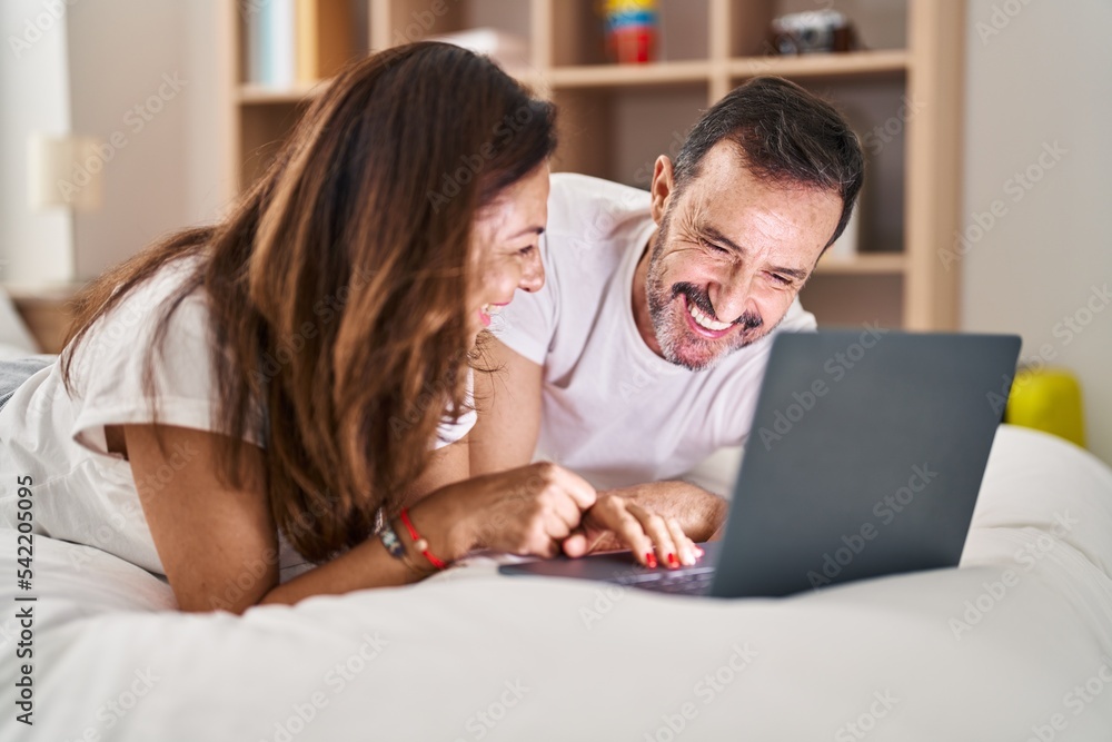 Middle age man and woman couple using laptop lying on bed at bedroom Middle age man and woman couple using laptop lying on bed at bedroom