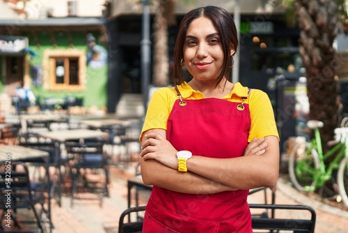 Young beautiful arab woman waitress smiling confident standing with arms crossed gesture at coffee shop terrace
