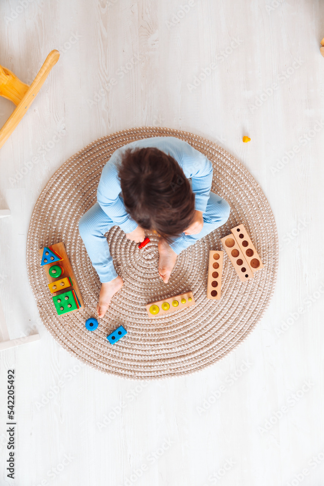 Naklejka premium a kid in pajamas is sitting on the floor in his room and playing with a wooden construction kit. natural toys for children. the boy is playing in his bedroom.