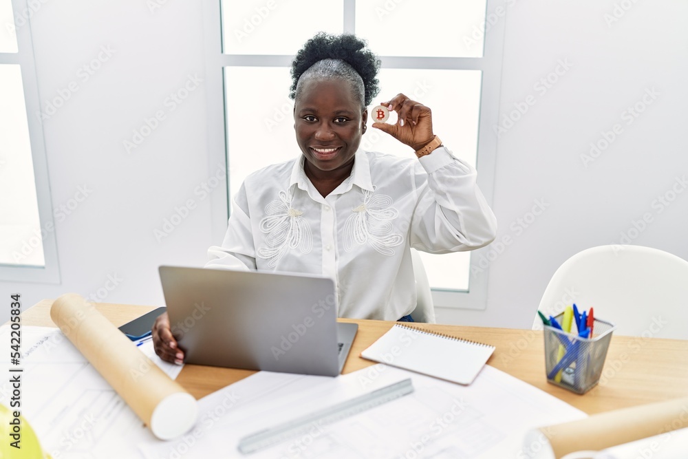 Young african american woman architect using laptop holding bitcoin at architecture studio Young african american woman architect using laptop holding bitcoin at architecture studio