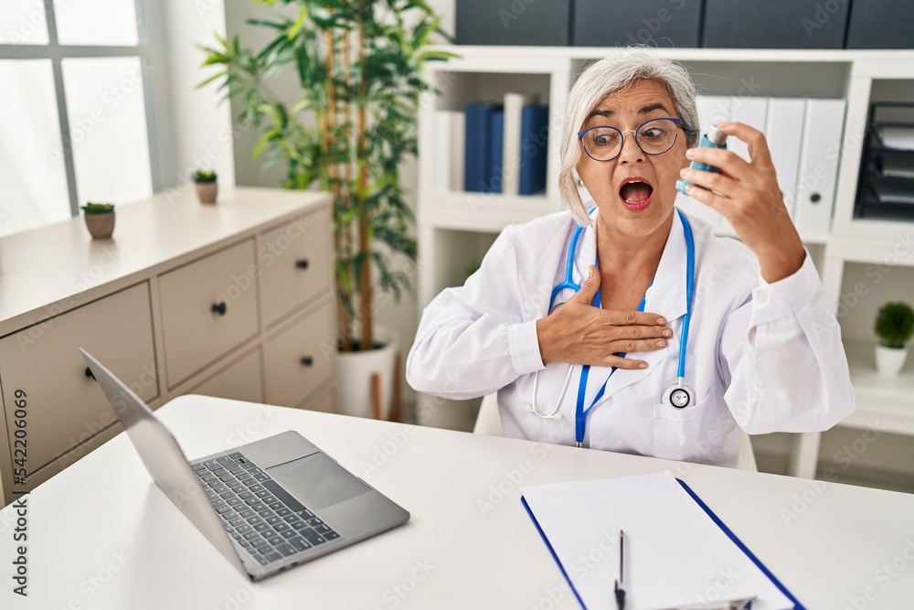 Middle age woman wearing doctor uniform holding inhaler at clinic Middle age woman wearing doctor uniform holding inhaler at clinic