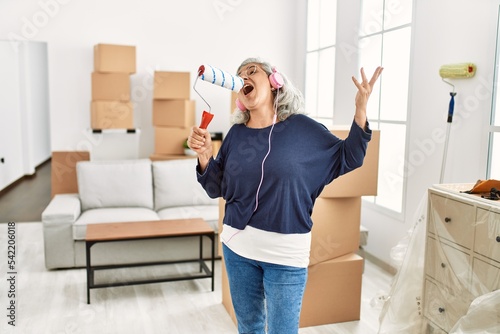 Middle age grey-haired woman listening to music and singing at new home.