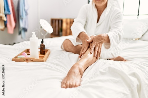 Woman caring skin legs using hydration cream sitting on the bed at bedroom.