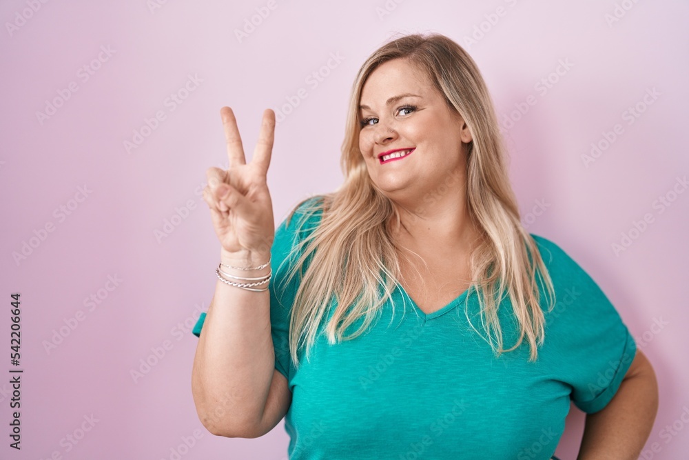 Caucasian plus size woman standing over pink background smiling looking to the camera showing fingers doing victory sign. number two. Caucasian plus size woman standing over pink background smiling looking to the camera showing fingers doing victory sign. number two.