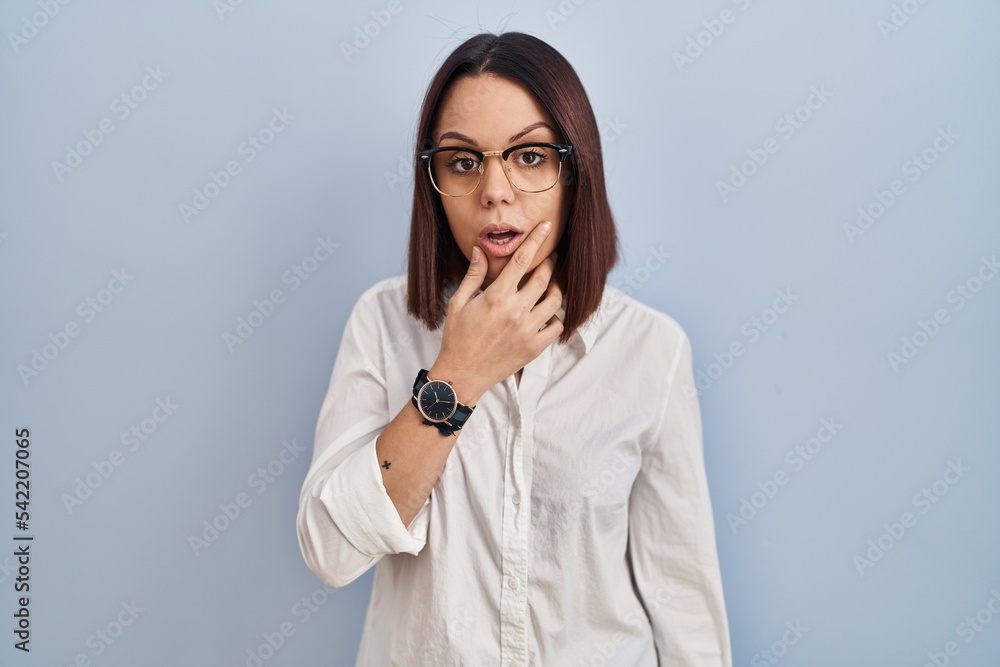 Young hispanic woman standing over white background looking fascinated with disbelief, surprise and amazed expression with hands on chin Young hispanic woman standing over white background looking fascinated with disbelief, surprise and amazed expression with hands on chin
