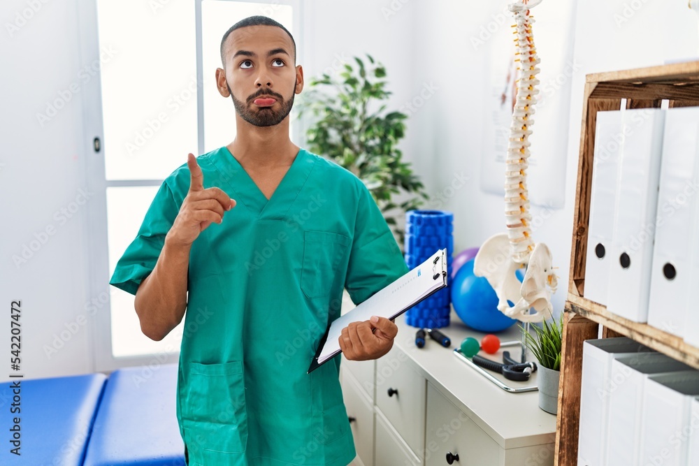 Fototapeta premium African american physiotherapist man working at pain recovery clinic pointing up looking sad and upset, indicating direction with fingers, unhappy and depressed.