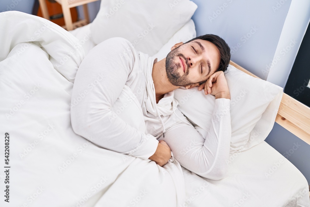 Fototapeta premium Young hispanic man lying on bed sleeping at bedroom