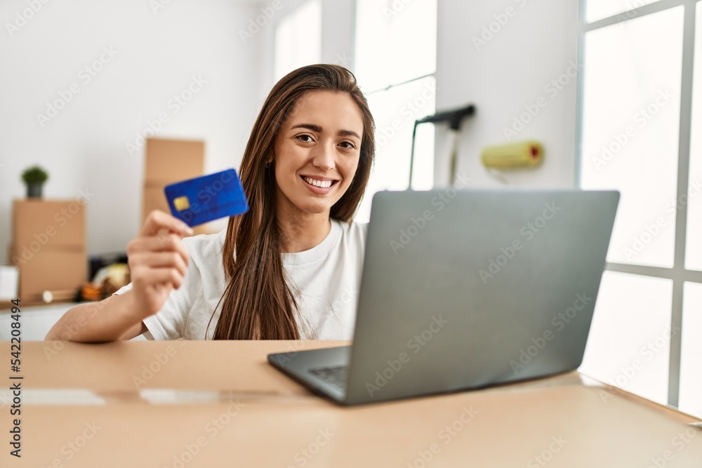 Young hispanic woman smiling confident using credit card and laptop at new home Young hispanic woman smiling confident using credit card and laptop at new home