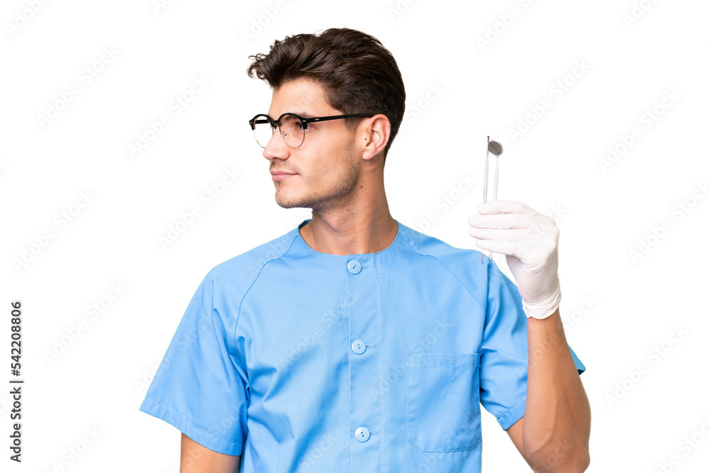 Young dentist man holding tools over isolated background looking to the side