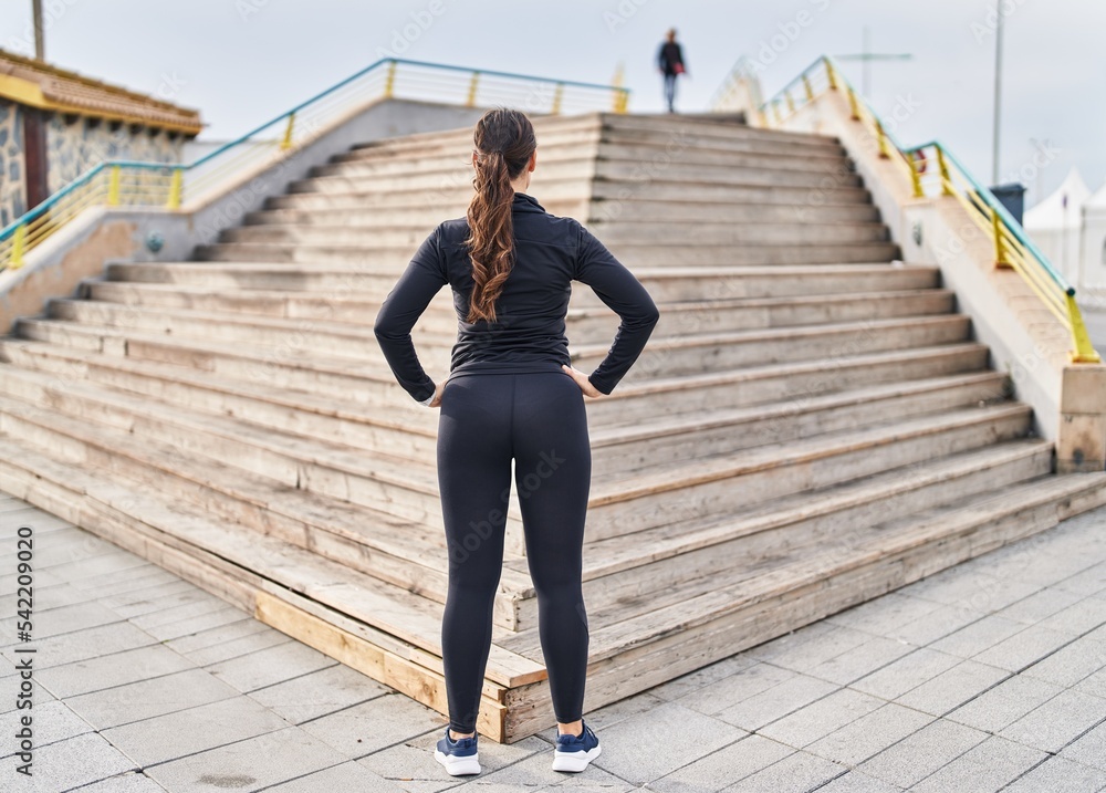 Young hispanic woman wearing sportswear standing on back view looking stairs at street