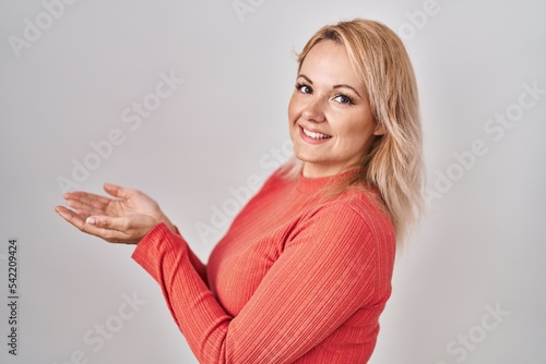 Blonde woman standing over isolated background pointing aside with hands open palms showing copy space, presenting advertisement smiling excited happy