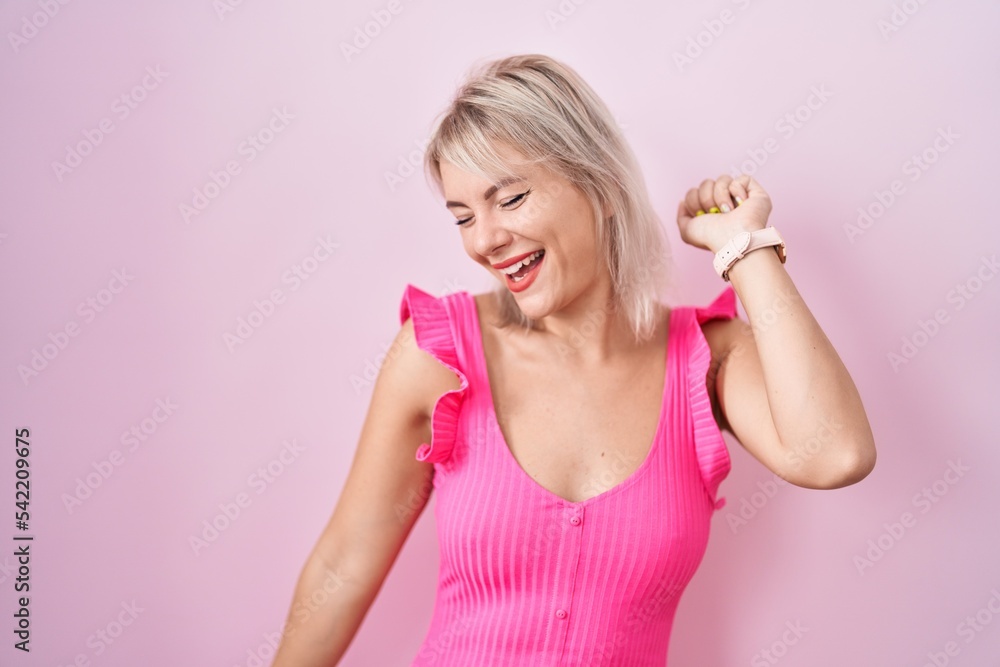 Young caucasian woman standing over pink background dancing happy and cheerful, smiling moving casual and confident listening to music Young caucasian woman standing over pink background dancing happy and cheerful, smiling moving casual and confident listening to music