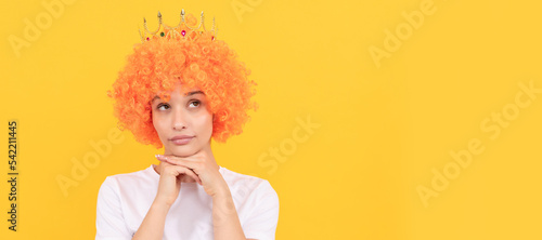 egoistic funny girl with fancy look wearing orange hair wig and princess crown, imagining. Woman isolated face portrait, banner with copy space.