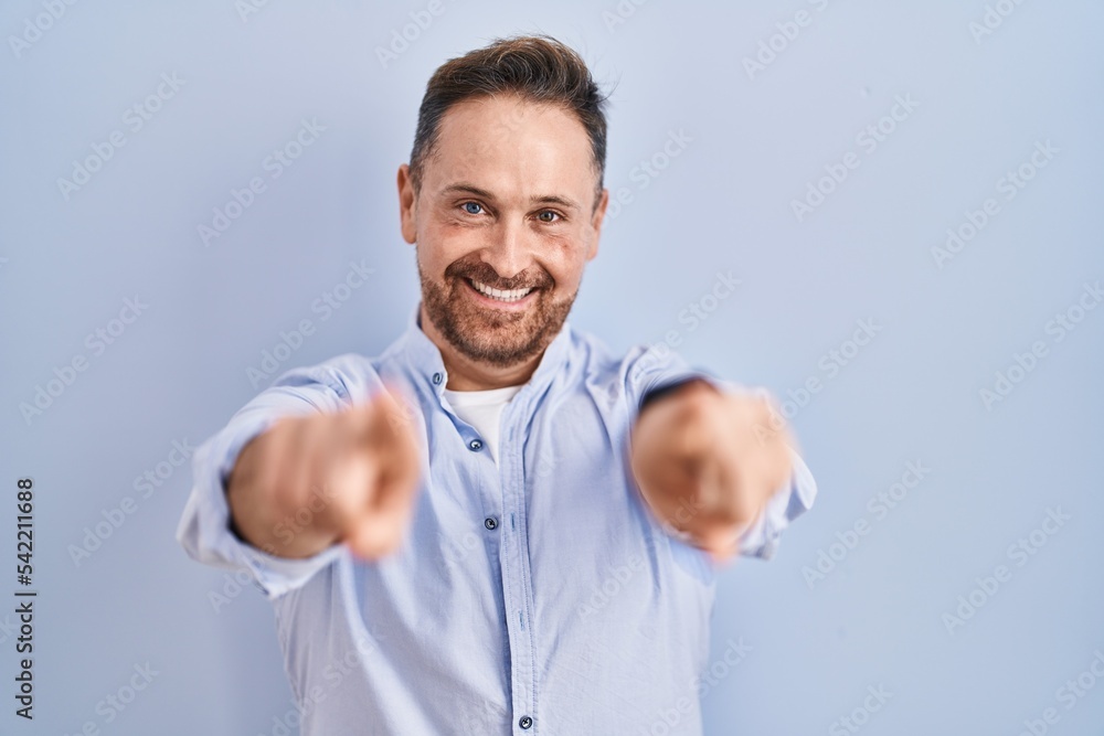 Middle age caucasian man standing over blue background pointing to you and the camera with fingers, smiling positive and cheerful Middle age caucasian man standing over blue background pointing to you and the camera with fingers, smiling positive and cheerful