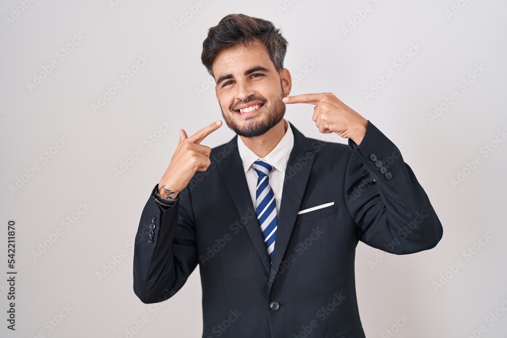 Young hispanic man with tattoos wearing business suit and tie smiling cheerful showing and pointing with fingers teeth and mouth. dental health concept. Young hispanic man with tattoos wearing business suit and tie smiling cheerful showing and pointing with fingers teeth and mouth. dental health concept.