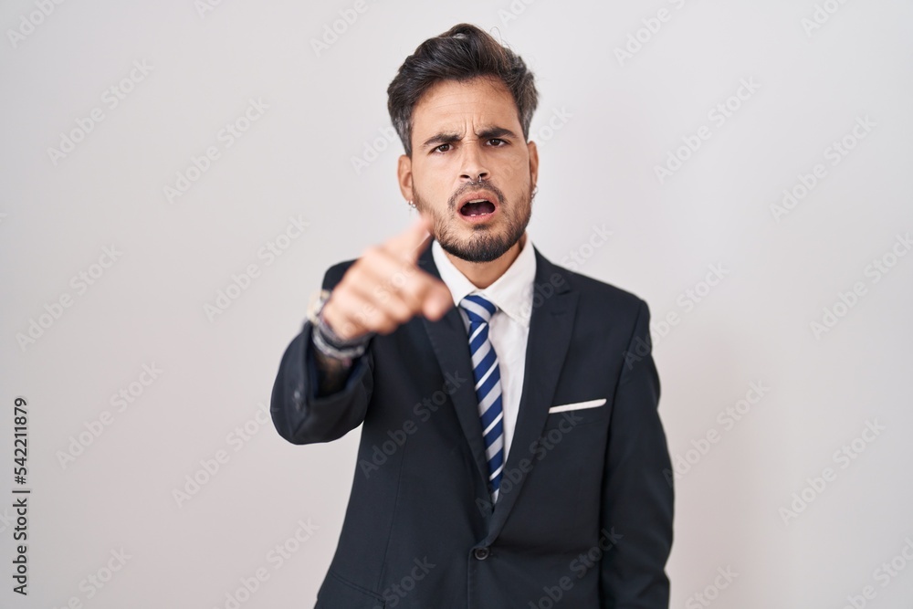 Young hispanic man with tattoos wearing business suit and tie pointing displeased and frustrated to the camera, angry and furious with you Young hispanic man with tattoos wearing business suit and tie pointing displeased and frustrated to the camera, angry and furious with you