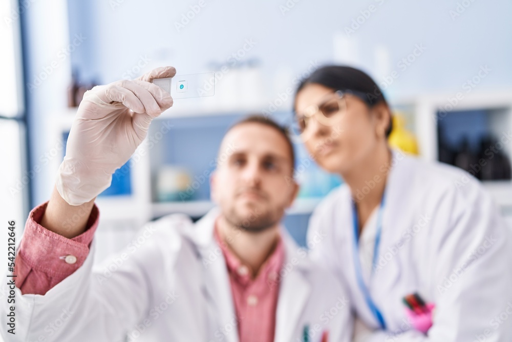 Man and woman wearing scientists uniform looking sample at laboratory Man and woman wearing scientists uniform looking sample at laboratory