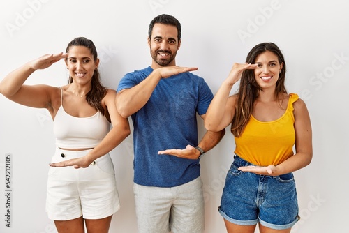 Group of young hispanic people standing over isolated background gesturing with hands showing big and large size sign  measure symbol. smiling looking at the camera. measuring concept.