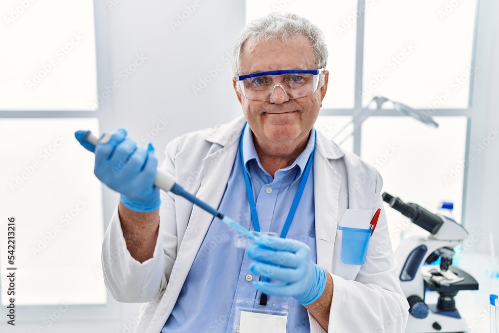 Middle age grey-haired man wearing scientist uniform using pipette at laboratory Middle age grey-haired man wearing scientist uniform using pipette at laboratory