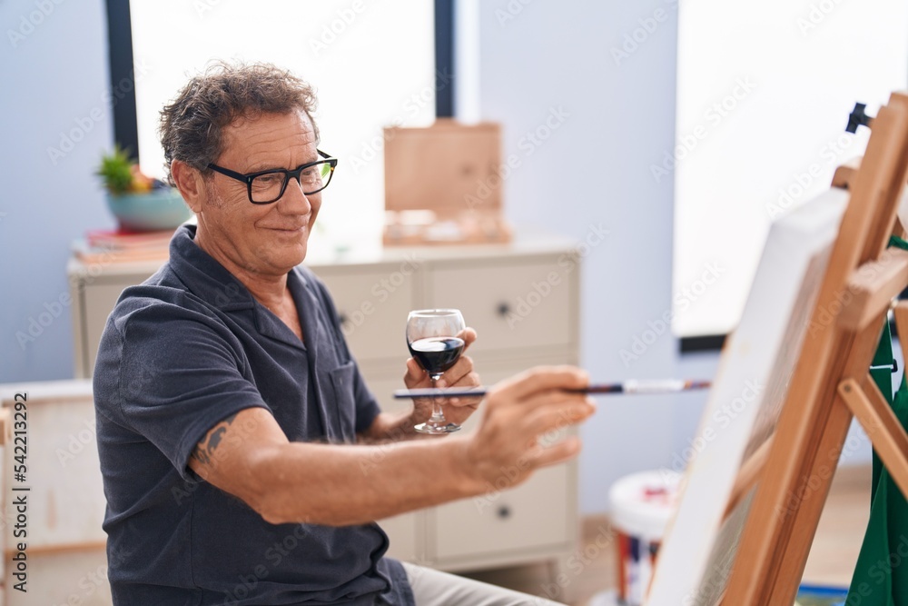 Middle age man artist drinking wine drawing at art studio