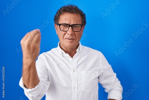 Middle age hispanic man standing over blue background doing italian gesture with hand and fingers confident expression