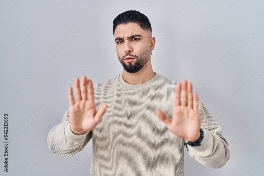 Naklejka premium Young handsome man standing over isolated background moving away hands palms showing refusal and denial with afraid and disgusting expression. stop and forbidden.