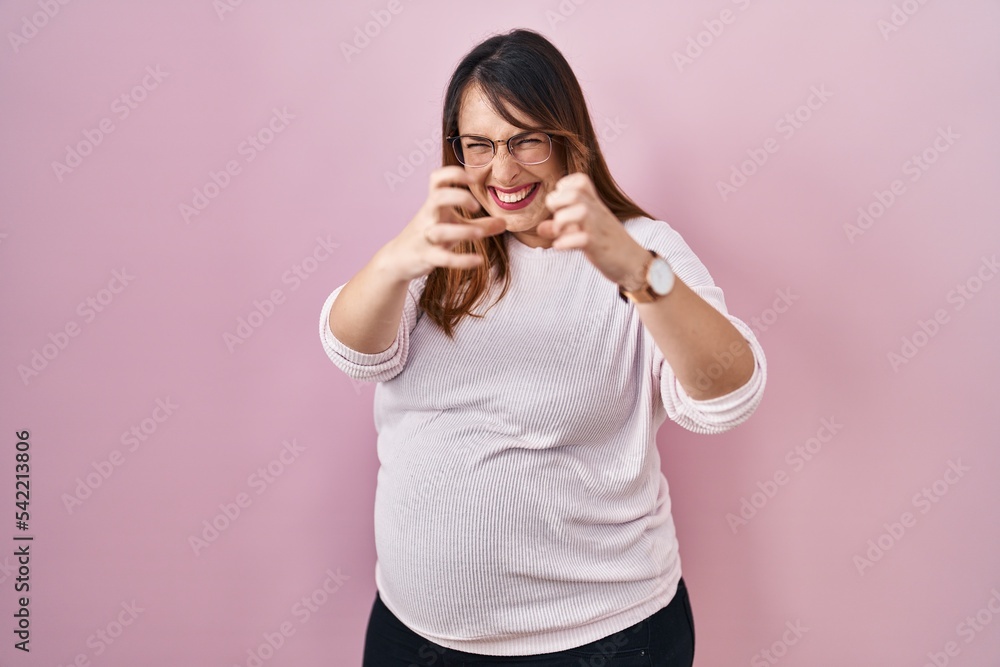 Pregnant woman standing over pink background shouting frustrated with rage, hands trying to strangle, yelling mad Pregnant woman standing over pink background shouting frustrated with rage, hands trying to strangle, yelling mad