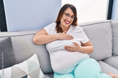 Free Download Young pregnant woman examining breast sitting on sofa at home - GFXLoad